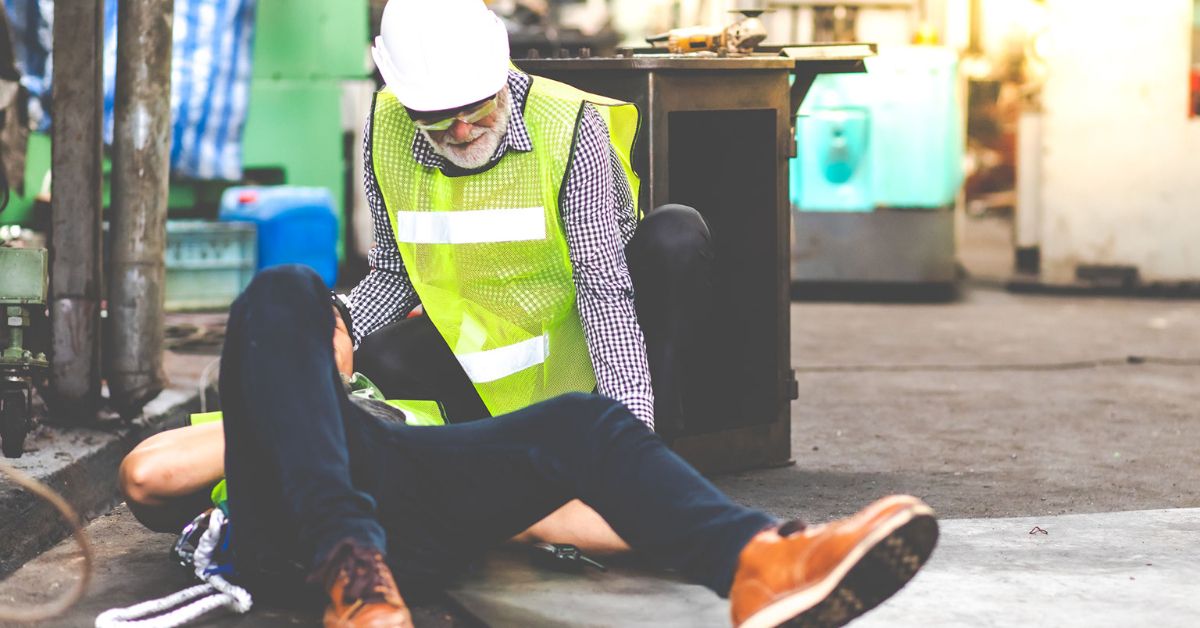 A man kneels next to a coworker who was hurt on the job until help arrives.